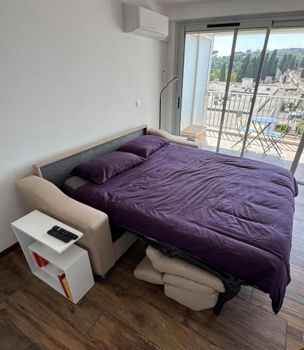 - une chambre avec un lit doté de draps violets et une fenêtre dans l'établissement Studio neuf avec terrasse vue mer, à Cannes