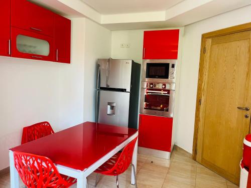 a kitchen with red cabinets and a red table and chairs at Résidence de standing , appartement à 2 pas de la mer , jardin, piscine Hammamet nord in Nabeul