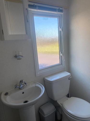 a bathroom with a sink and a toilet and a window at Coastal Chalet in Tudweiliog- Tyddyn Mawr in Pwllheli