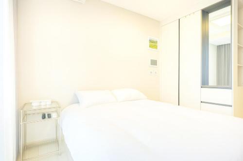 a white bedroom with two beds and a window at EL Stay Hotel Residence in Busan