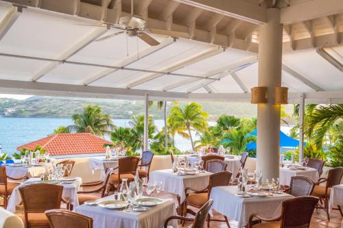 a restaurant with white tables and chairs and the ocean at St. James's Club Resort - All Inclusive in English Harbour Town