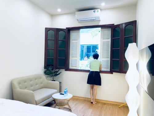 Una donna che guarda fuori da una finestra in una camera da letto di Cozy Oasis - Gần Hồ Hoàn Kiếm a Hanoi