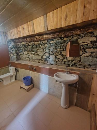 a bathroom with a sink and a stone wall at Zayru Cottage & cafe in Jibhi