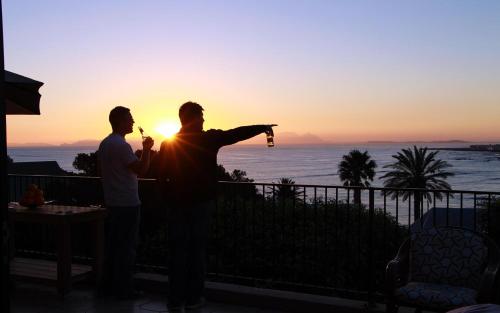 two men standing on a balcony watching the sunset at Die Braaihuis, sleeps 6, Central and Fabulous! in Gordonʼs Bay