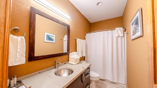 a bathroom with a sink and a toilet and a mirror at The Cove - 3-Bedroom, 3-Bathroom Penthouse Suite at REAL Watersports in Waves
