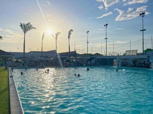 people swimming in a pool with palm trees and the sun at Decifer Sport Resort in Belas