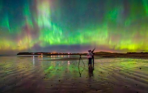 a person standing on the beach under the northern lights at The Den - by Caithness Luxury Apartments NC500 - 2 Bedroom holiday home - Sleeps Work teams upto 2 & holiday makers upto 4 in Wick