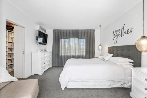 a white bedroom with a large bed and a tv at Airport Oasis in Rotorua