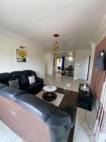 a living room with a black leather couch and a table at Appartement meublé spacieux 2 chambres salon Yassa in Douala