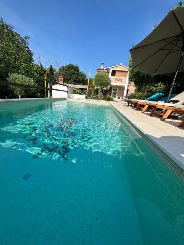 a large blue swimming pool with an umbrella and benches at Wellness House Oliva, Heated Pool, Sauna and Jacuzzi in Labin