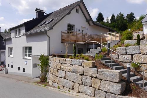a white house with a stone retaining wall at First Class Domizil Großer Bergzauber inklusive MeineCardPlus in Willingen