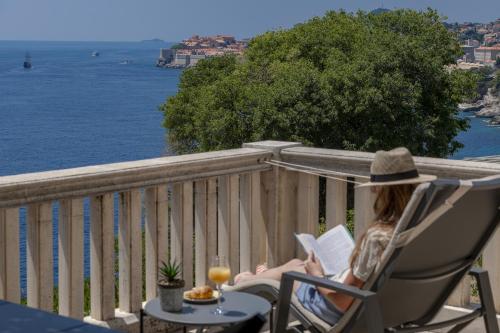 a woman sitting in a chair reading a book at Apartments Kirigin in Dubrovnik