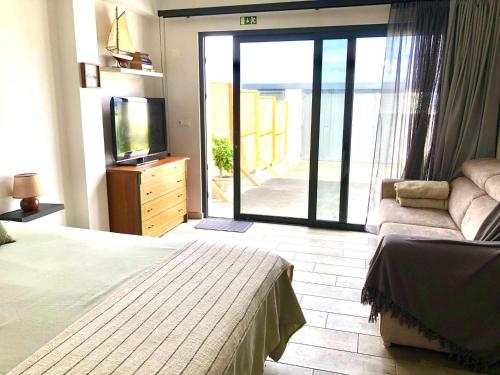 a bedroom with a bed and a television and a balcony at Seacrets Beach House in Praia do Almoxarife