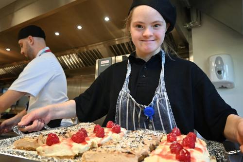 a woman in a kitchen with a cake with strawberries on it at Foxes Hotel in Minehead
