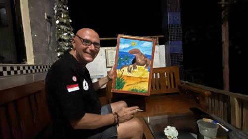 a man holding up a painting of a bird at Tarsan Homestay in Labuan Bajo
