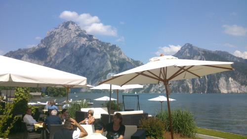 a group of people sitting at tables under umbrellas near the water at Bernhard Schmidt-Gasse in Gmunden