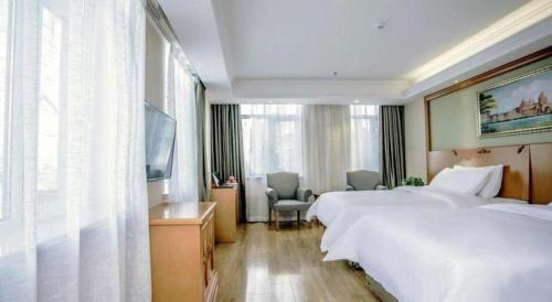a hotel room with two beds and a desk and a television at Vienna Hotel Inner Mongolia Tongliao Development Zone in Tongliao