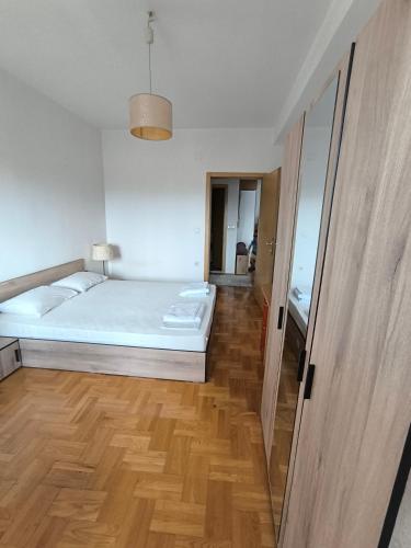 a white bedroom with a bed and a wooden floor at D Center Apartment in Kumanovo