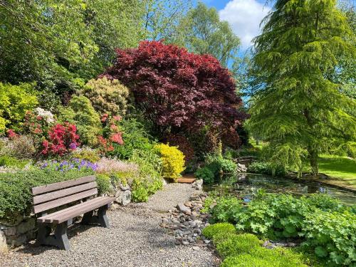 un banco de parque en un jardín con flores y un estanque en Forge Mill Cottage, en Dalbeattie