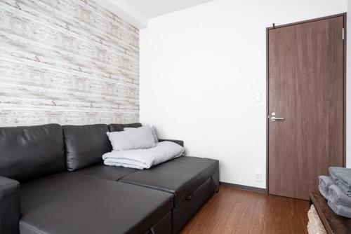 a living room with a black leather couch and a wooden door at 3ベッドルームとリビング 4部屋全て個室 混まない2つのシャワールームとトイレ 東新宿駅2分8名 in Tokyo
