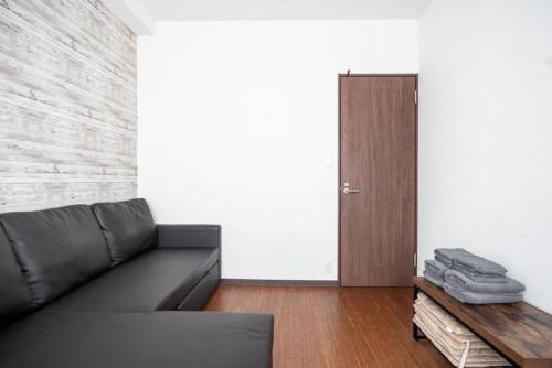 a living room with a black leather couch and a door at 3ベッドルームとリビング 4部屋全て個室 混まない2つのシャワールームとトイレ 東新宿駅2分8名 in Tokyo