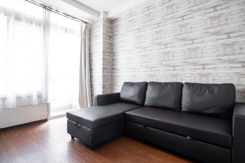 a living room with a black couch and a brick wall at 3ベッドルームとリビング 4部屋全て個室 混まない2つのシャワールームとトイレ 東新宿駅2分8名 in Tokyo