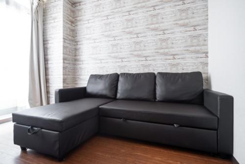 a black leather couch in a room with a wall at 3ベッドルームとリビング 4部屋全て個室 混まない2つのシャワールームとトイレ 東新宿駅2分8名 in Tokyo