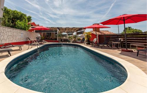 a swimming pool with red umbrellas on a patio at Nice Home In Turanj With Jacuzzi in Turanj