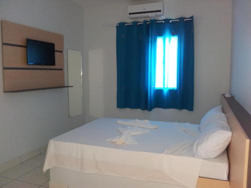 a bedroom with a white bed with a blue curtain at Hotel Cavalo Marinho Suítes in Caraguatatuba