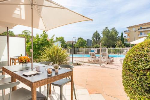 un patio avec une table, des chaises et un parasol dans l'établissement Appart'City Classic Aix-en-Provence - La Duranne, à Aix-en-Provence