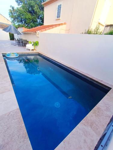 une piscine d'eau bleue devant un mur blanc dans l'établissement Maison paisible et spacieuse, à Sorgues