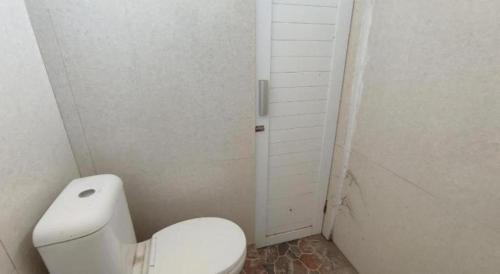 a white bathroom with a toilet and a door at Hotel O Wisma Sidosari Syariah in Bandar Lampung