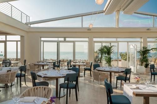 a restaurant with tables and chairs with the ocean in the background at Bellevue Sardinia Resort Affiliated by Meliá in Valledoria