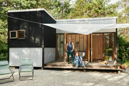 ein Mann und ein Mädchen sitzen auf der Veranda eines winzigen Hauses in der Unterkunft Off-Grid Summer Pavilion With Views Of Gotlands Nature in Lärbro