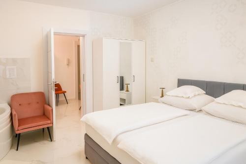 a white bedroom with a bed and a chair at Royal Wellness Apartman in Hévíz