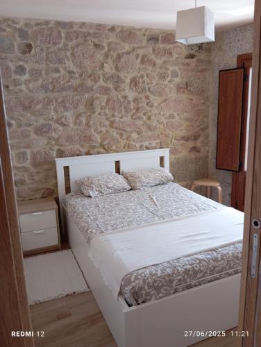 a bedroom with a white bed with a stone wall at Casa de piedra céntrica. in Ribeira
