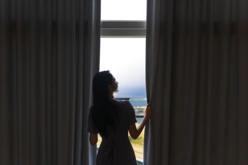 a woman looking out a window at the ocean at DIAMER Hotel Sokcho by AankStay in Yangyang