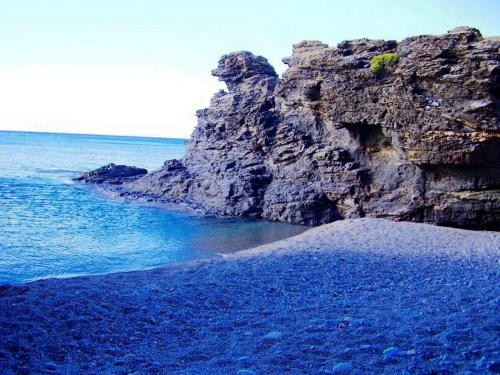 a rocky beach with blue water and a rocky cliff at Saint George Hotel in Rodakino