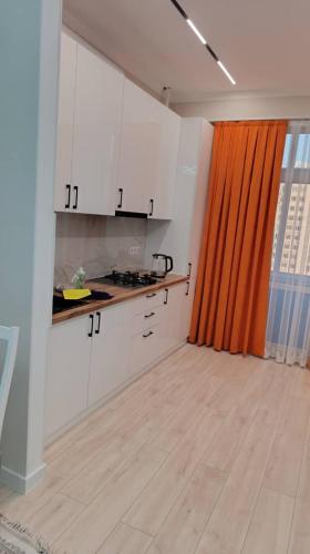 a kitchen with white cabinets and an orange curtain at Elit in Bishkek