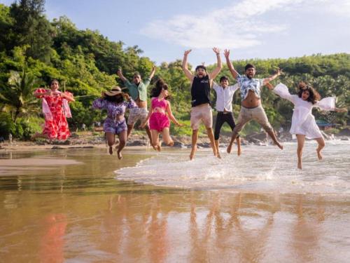 a group of people jumping in the water on the beach at The Hosteller Gokarna in Gokarna