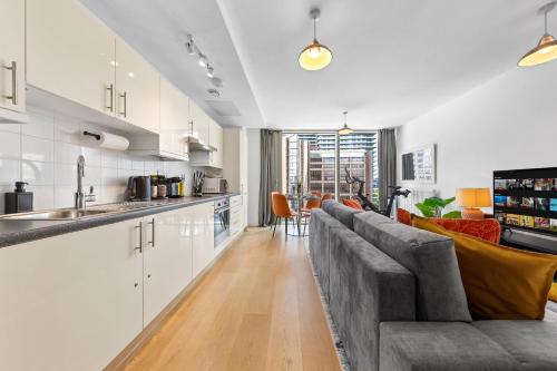 a living room with a gray couch and a kitchen at Canary Wharf Apartment in London