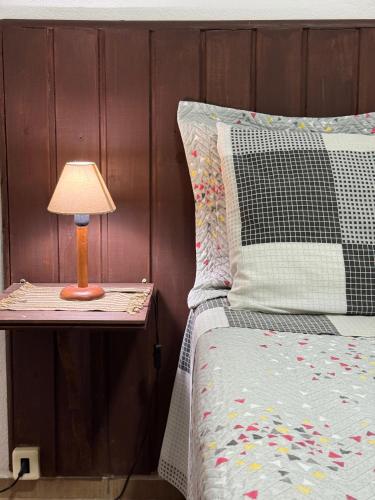 a bed with a table with a lamp on it at Chalé Topázio in Monte Verde