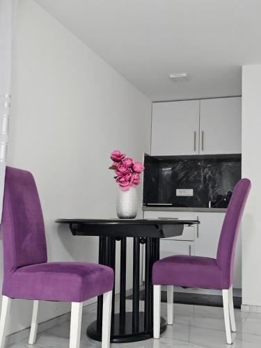 a table with purple chairs and a vase of flowers at Studio Dana in Arandjelovac