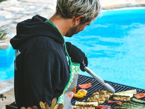 a man cooking food on a grill next to a pool at Da Silva Surfcamp - Tiny House Jorgina in Lourinhã