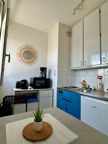 une cuisine avec des armoires bleues et une table avec une plante dans l'établissement Studio - Arc En Ciel 1 - 23 allée des pinons - 5-1, à Saint-Jean-de-Monts