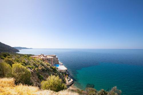 a house on a hill next to a body of water at Teulada cozy flat with pool and beach access in Teulada