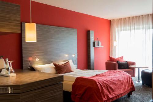 a bedroom with a red wall with a bed and a desk at Atrium Hotel Mainz in Mainz
