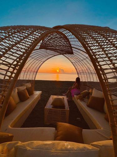 a woman sitting on a couch under an archway with the sunset at Beach Hive Seafront Villa at San Juan Batangas in Batangas City