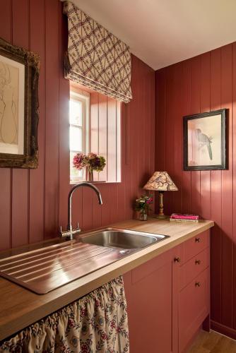 a kitchen with red walls and a sink and a window at Haybarn Cottage in Alton