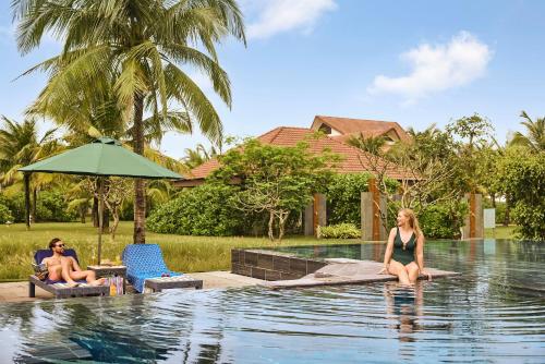 two people sitting on the edge of a swimming pool at ROBINSON Nam Hoi An in Tam Ky